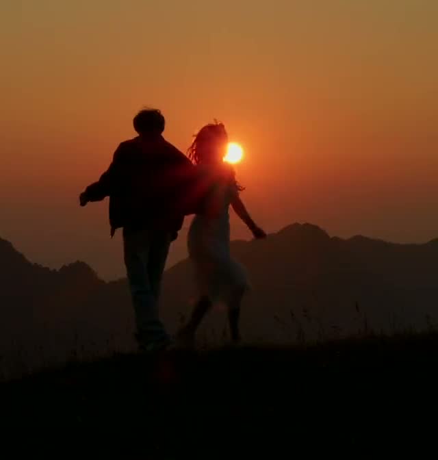 A couple dancing on a ridge at sunset, in silhouette