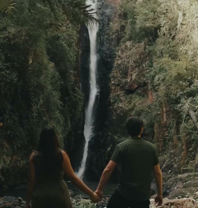 A couple holding hands in front of a waterfall
